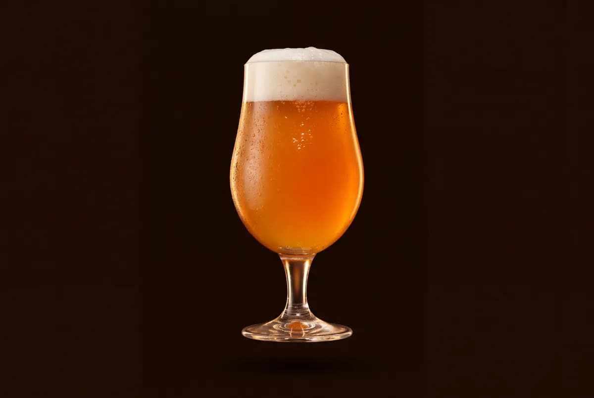 Verre tulipe rempli d’une IPA orangée et voilée, sous un col de mousse blanche.
