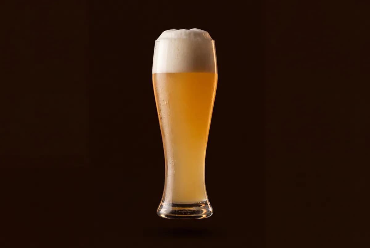 Verre de bière blanche trouble sous un col de mousse dense.