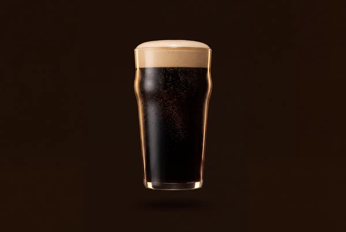Verre de stout noire opaque surmonté d’une mousse crémeuse beige au dôme lisse.