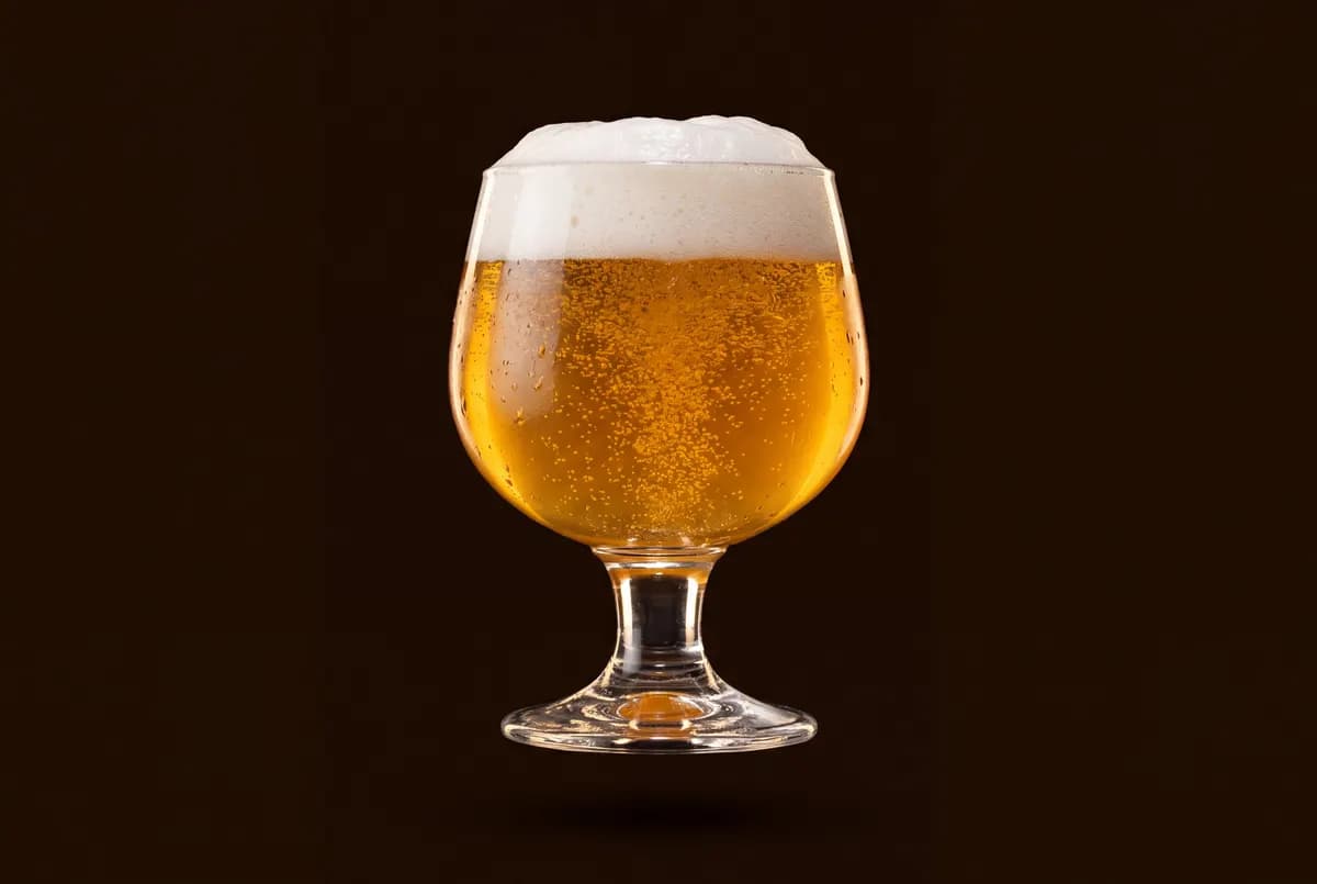 Calice sur pied rempli d’une bière dorée très effervescente, mousse blanche débordant du bord.